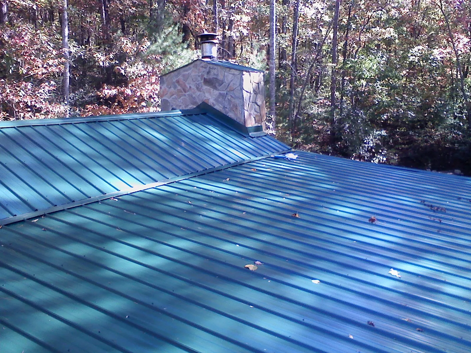 New green metal roof and stone chimney surrounded by autumn woods in Waco