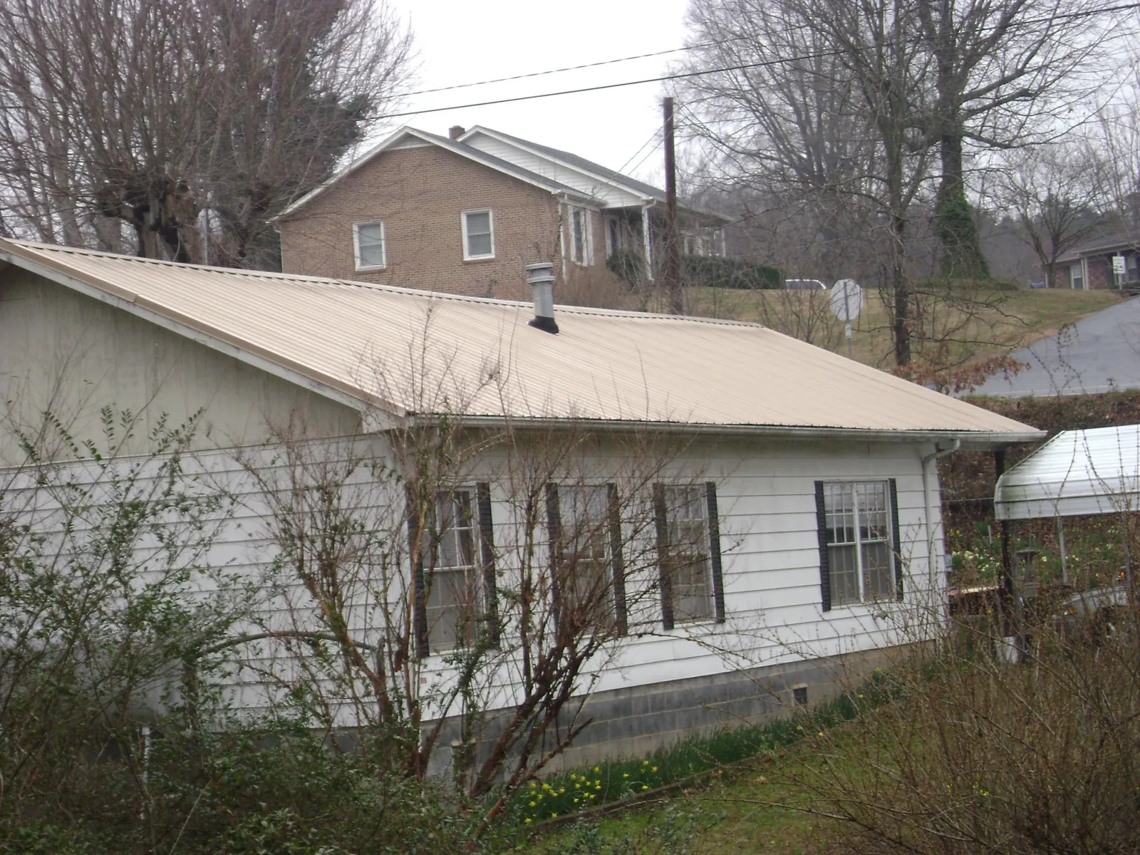 Tan metal roof on a white sided house set into a hillside — Commercial Roofing by Roofing Brothers in Waco